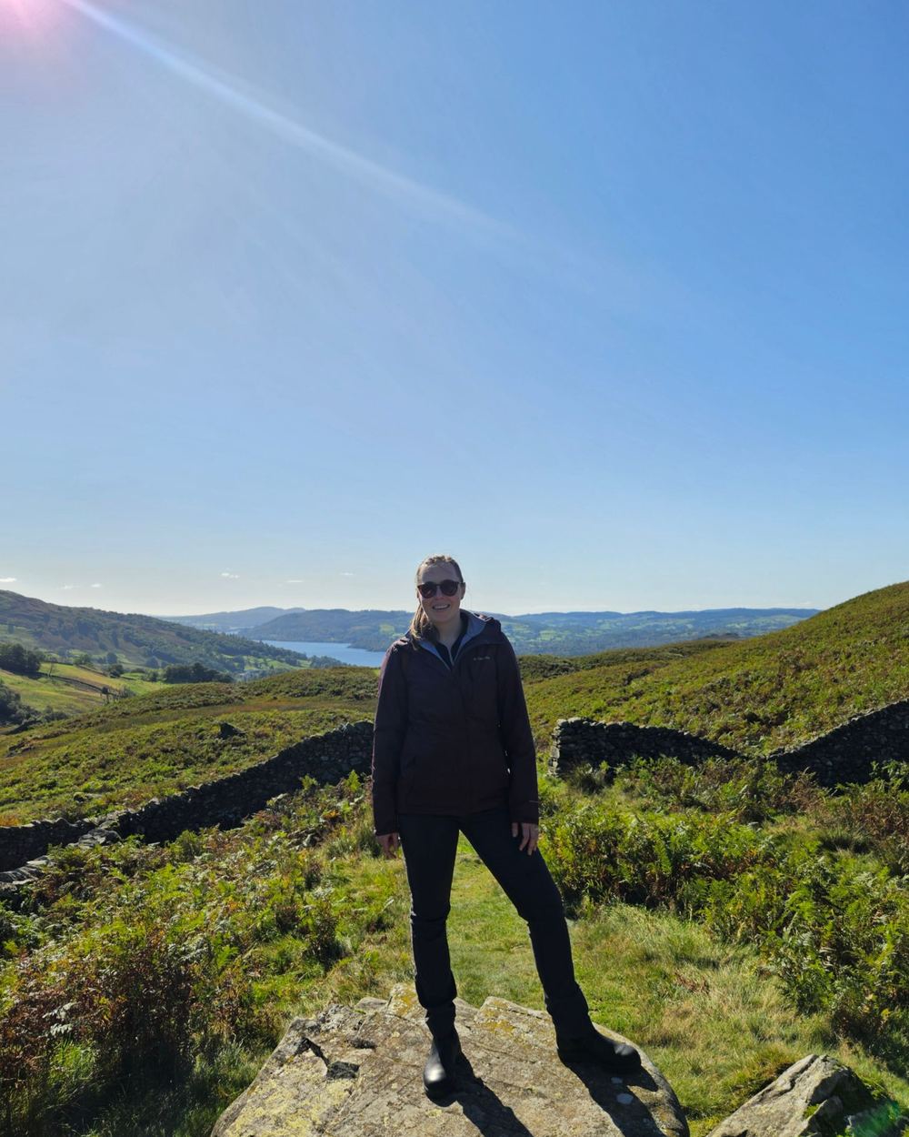 Alaina standing on a rock in green fells above a lake on a sunny day