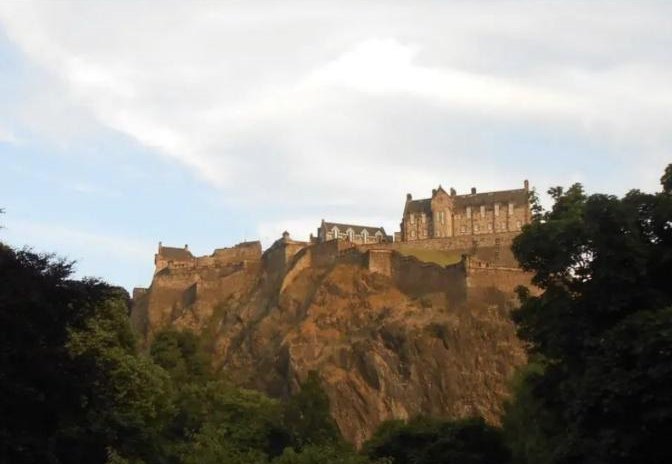 Edinburgh Castle on its rock above the trees, lit by evening sun