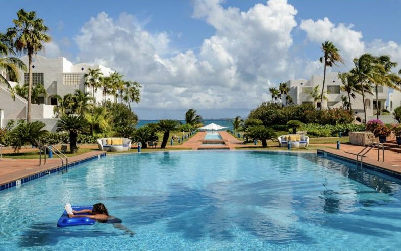 A long resort swimming pool lined with palm trees under a summer sky