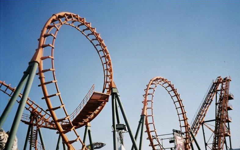 Looping orange roller coaster track against a clear blue sky